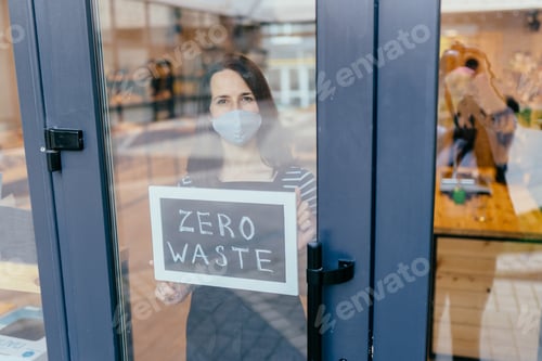 Preview: Tired sad woman small business owner in fasial mask holds sign with inscription zero waste