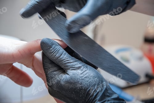 Preview: Skilled manicure master using fingernail file while correcting client nail form