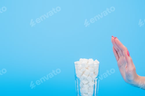 Preview: cropped view of woman refusing from white sugar cubes in glass isolated on blue