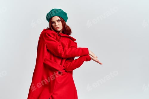 Preview: A woman holds in her hand a red coat and a dark T-shirt Green hat cropped view of a light background