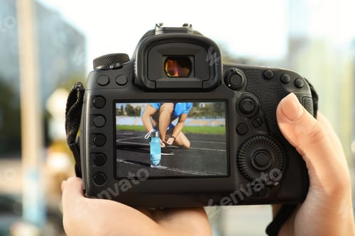 Preview: Female photographer holding professional camera with picture on screen outdoors, closeup