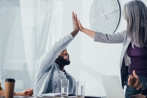 Preview: smiling multicultural colleagues giving high five in office