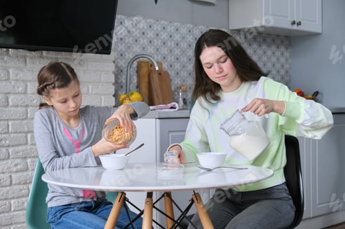 Preview: Girls having breakfast sitting at table in home kitchen
