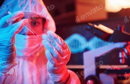 Preview: Nurse in mask and white uniform, holding tube with liquid and sitting in neon lighted laboratory