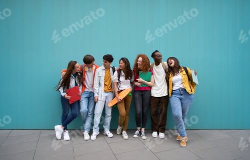 Preview: Large group of cheerful young people leaning against blue wall. Multicultural college students.