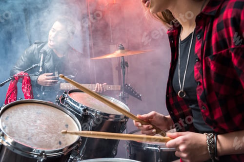 Preview: side view of woman playing drums and man singing into microphone, rock and roll band concept