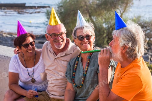 Preview: group of seniors and mature people sitting at the beach with party's cap