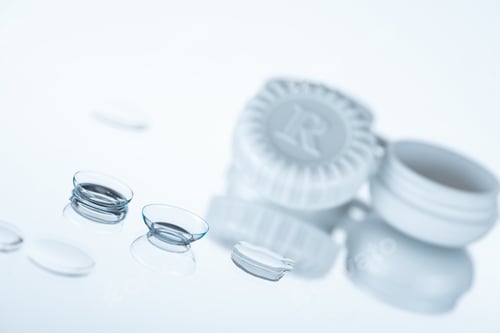 Preview: selective focus of contact lenses and container on white backdrop