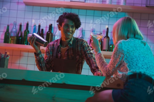 Preview: selective focus of smiling african american barman shaking cocktail while listening to woman in bar