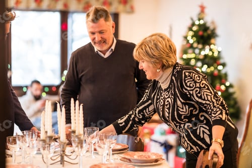 Preview: Family arranging christmas dinner table with candles in cozy home