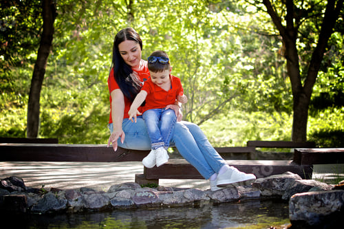 Preview: Young turk woman and little boy sitting by the pond in the summer park