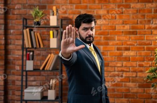 Preview: Frustrated Indian CEO signals stop using hand while standing in cozy corporate workspace