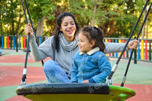 Preview: Happy Latin mother playing with her son on a swing in a park.