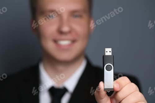 Preview: Man with usb flash drive against grey background, focus on device. Space for text