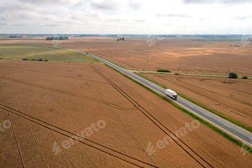 Preview: view from above to a ripe wheat field with a asphalted road to the right on a sunny day in autumn