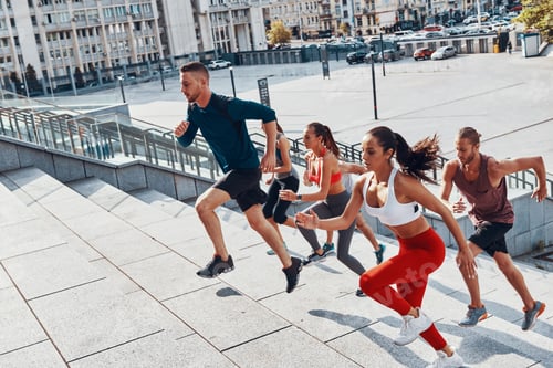 Preview: Group of young people in sports clothing jogging while exercising on the stairs outdoors