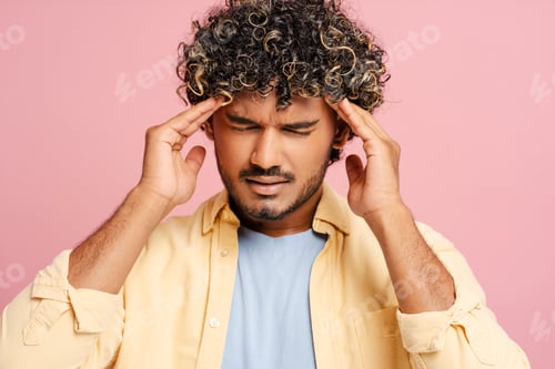Preview: Sick Indian man suffering from a headache is touching his temples on pink background