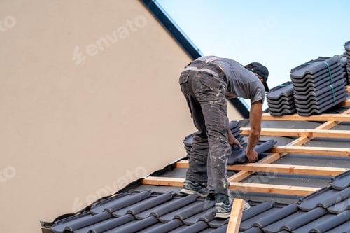 Preview: roofer installs a fired ceramic tile on the roof of family house
