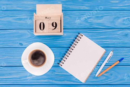 Preview: top view of wooden calendar with date of 9th may, coffee cup, blank textbook and pens, victory day