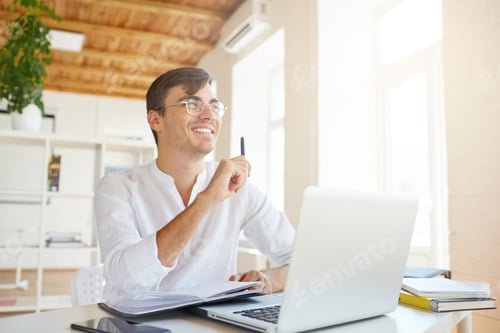 Preview: young businessman wears white shirt and spectacles with laptop and mobile phone thinking and writing