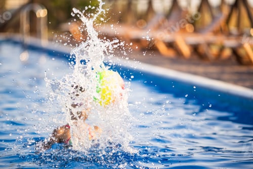 Preview: A girl in a bright bathing suit swims with an inflatable ball in a pool with clear water