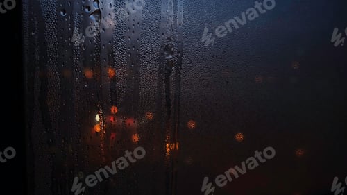 Preview: Close-up of the raindrops falling down on the glass and blurred light spots through the window at