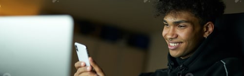 Preview: Distraction. Portrait of happy male student smiling and using smartphone while studying, working on