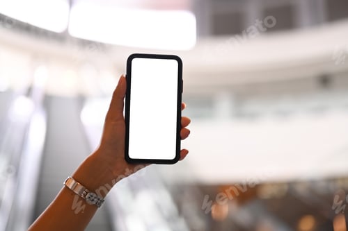 Preview: Cropped image of woman hand holding smart phone against blurred escalator background.