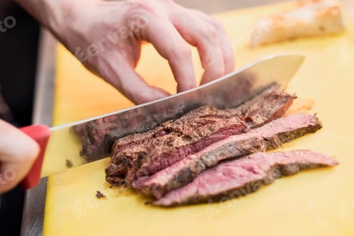 Preview: High angle close up of chef slicing beef with kitchen knife.