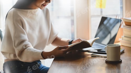 Preview: Cropped shot woman reading book on wooden table.