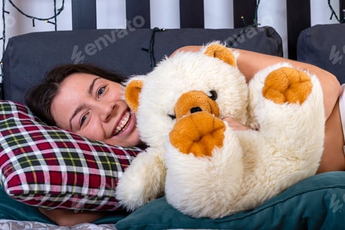 Preview: attractive smiling happy young woman hugging her teddy bear at bedroom
