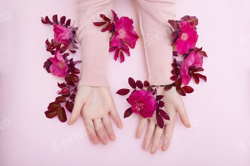 Preview: Hand with pink flowers and petals lying on a paper background. Cosmetics for hand