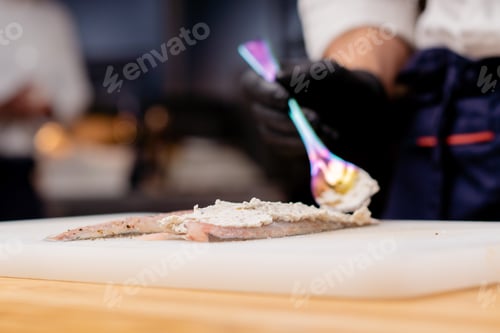 Preview: close-up of a chef's hands putting white sauce on fish with chrome spoon