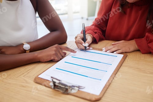 Preview: Two unknown ethnic business woman sitting together and signing office contract. African american pr
