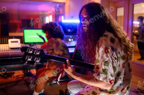 Preview: Male bass player is recording a song in a music studio while a technician is using mixing console.