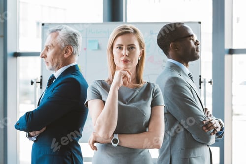 Preview: confident businessman standing with hand on chin and looking at camera while multiethnic businessmen