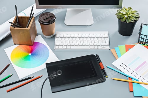 Preview: The gray desk with laptop, notepad with blank sheet, pot of flower, stylus and tablet for retouching