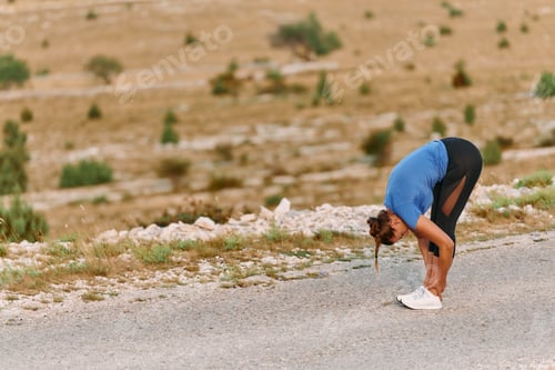 Vista previa: Determined Female Athlete Stretching After an Intense Run Through Rugged Mountain Terrain.
