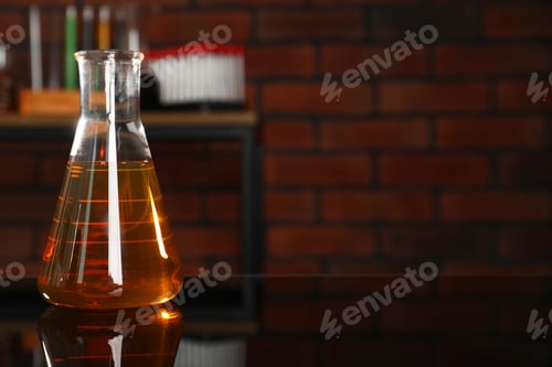 Preview: Flask with yellow oil on black mirror table indoors, closeup. Space for text