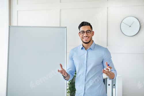 Preview: Joyful young Arab male teacher giving online private lesson from home, standing near empty