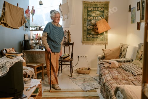 Preview: Senior Caucasian Woman Standing with Cane in Modest Home Interior Setting