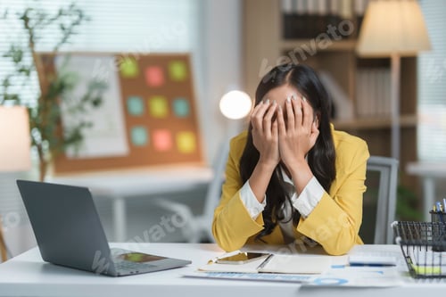 Preview: Stressed asian businesswoman covering face with hands while sitting at desk