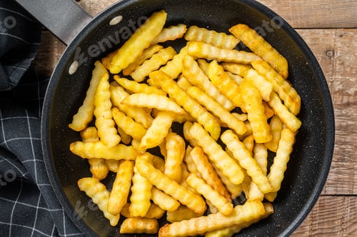 Preview: Fried Crinkle oven French fries potatoes sticks in a pan. Wooden background. Top view