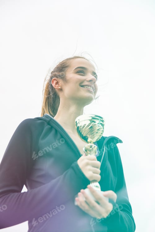 Preview: Happy sporty young woman holding gold trophy cup