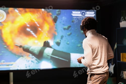 Preview: Man standing up in front of ultrawide screen, playing videogame using controller
