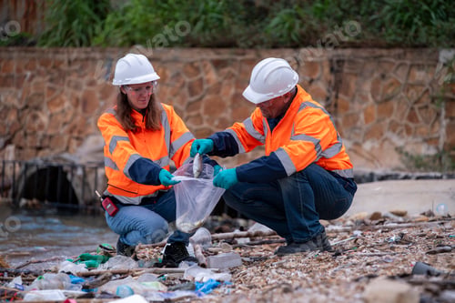 Preview: Environmental scientists or workers, wearing safety helmets and gloves, examining waste materials al