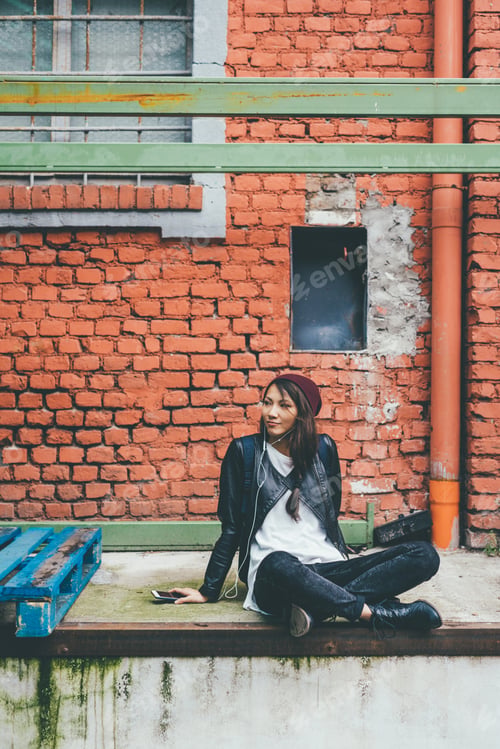 Preview: Young beautiful asiatic woman sitting listening music with earphones and smart phone