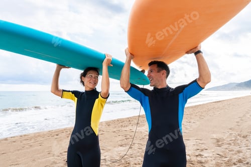 Preview: Couple carrying surfboards overhead on beach