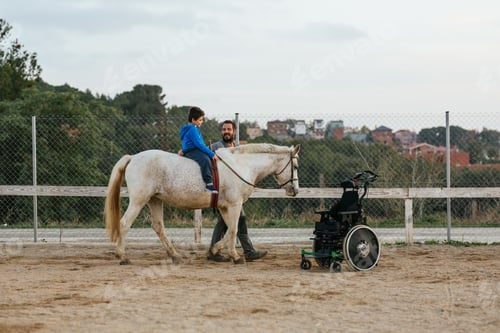 Preview: Physiotherapist and boy with disability on horse next to a wheelchair
