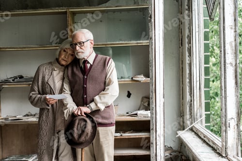 Preview: retired woman and bearded husband standing in damaged classroom